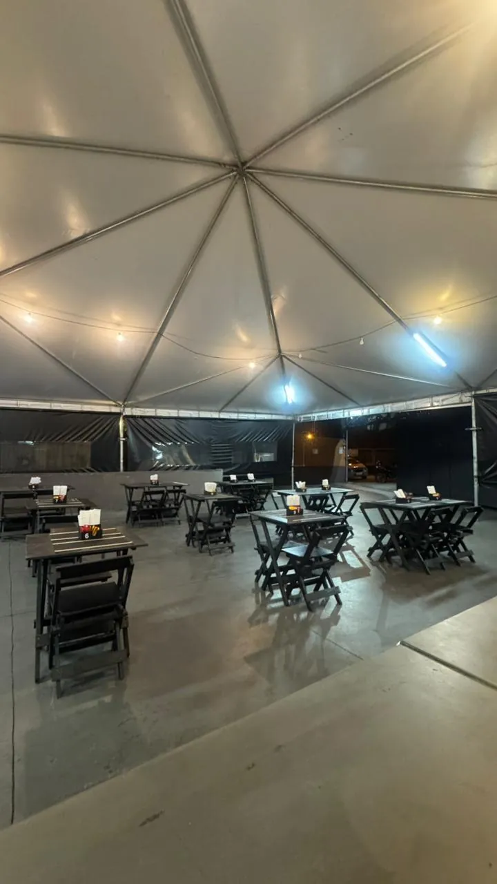 Salão coberto por tenda, com mesas e cadeiras de madeira escura